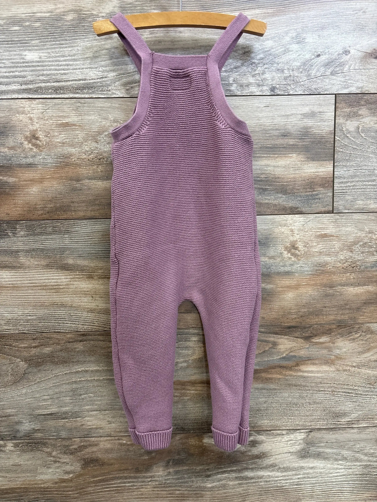 Front view of mauve Little Planet knit overalls, size 18m, showcasing bib front and ribbed cuffs with wood plank background
