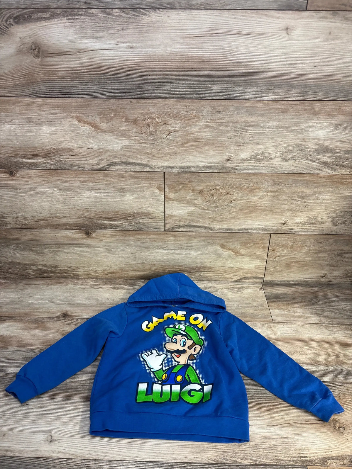Flat lay of blue toddler Luigi pullover hoodie showing large GAME ON and LUIGI back graphic with Luigi character on wood floor