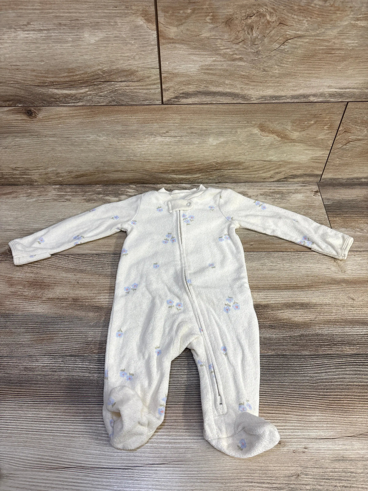 Front view of Carter’s cream terry cloth sleeper with footed legs, long sleeves, front zipper, and floral print on wood flooring