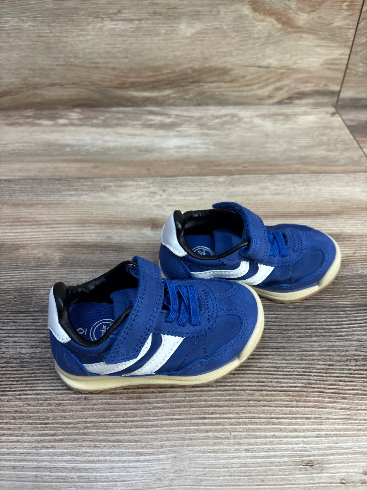 Three quarter view of toddler blue sneakers with white side stripes and Velcro strap on wood background, size 6C