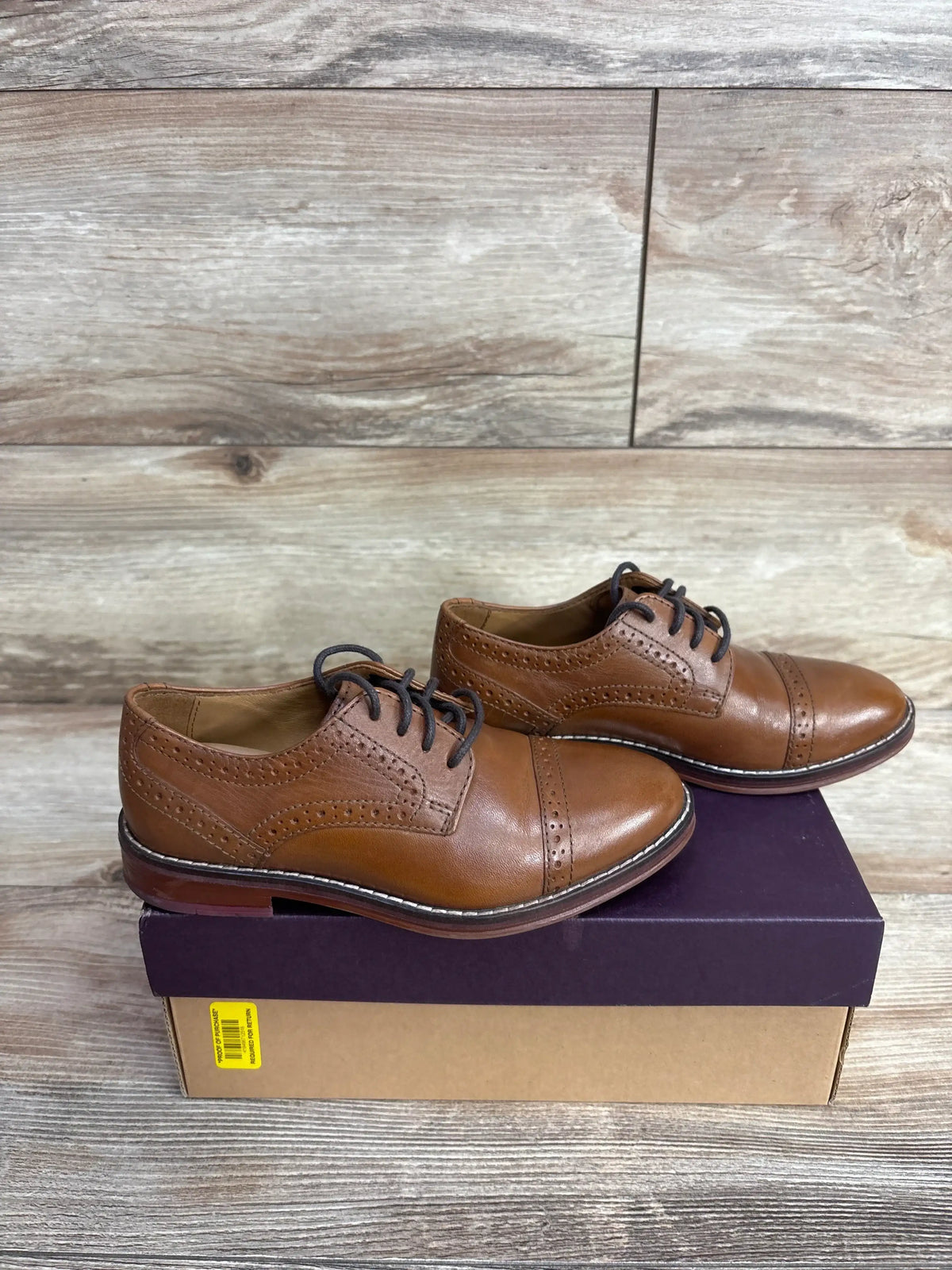 Pair of brown leather brogue shoes with black laces on a two-tone shoebox on wooden floor