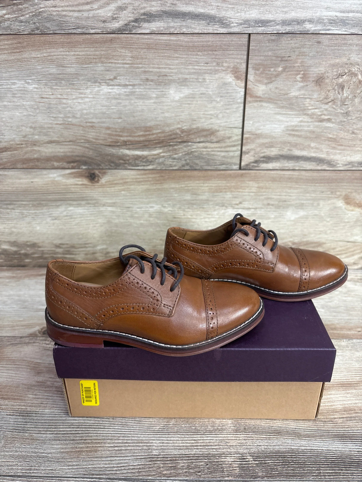 Pair of brown leather brogue shoes with black laces on a two-tone shoebox on wooden floor