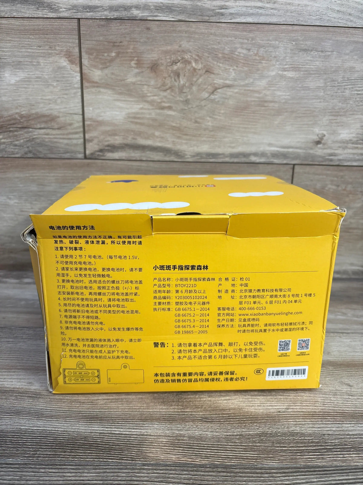 Back view of Banban’s Finger Forest toy box showcasing Chinese safety information with worn corners on wood-look flooring