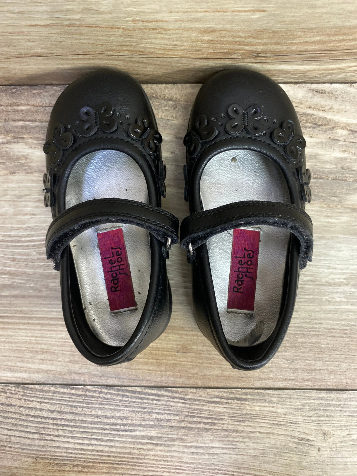 Black toddler Mary Jane shoes with floral accents and hook-and-loop strap on wood floor