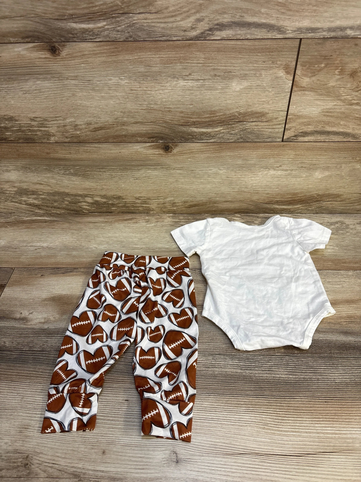 Baby outfit with white football print pants and plain white bodysuit on wood floor