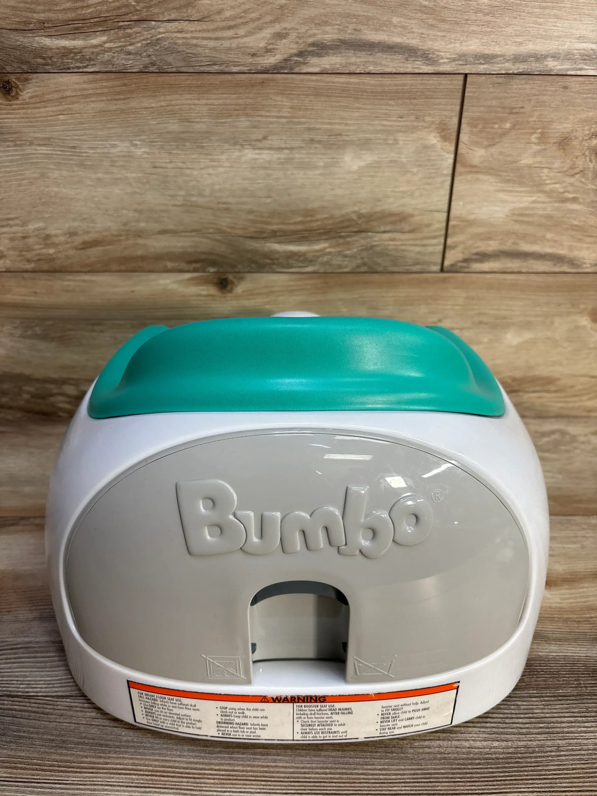 Rear view of Bumbo Multi Seat showcasing teal backrest and safety label against wood background