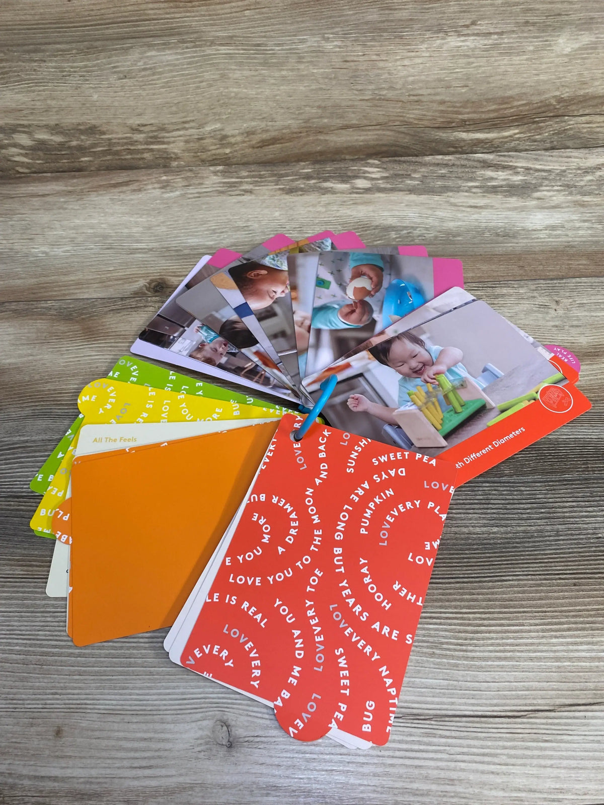 Colorful LovEvery flashcards with baby photos fanned out on a wooden surface