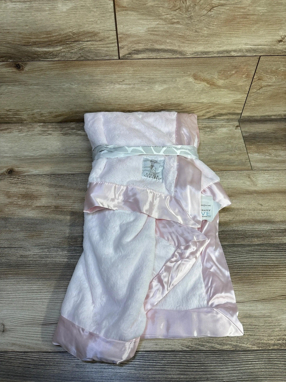 Top-down view of Little Giraffe Luxe baby blanket folded to show pink plush fabric and satin ribbon trim on a wood background