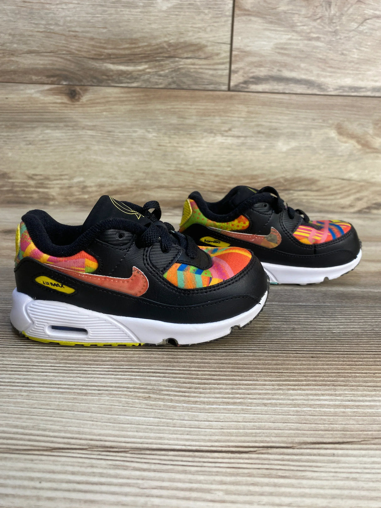 Colorful toddler Nike Air Max sneakers with black overlays on a wood floor