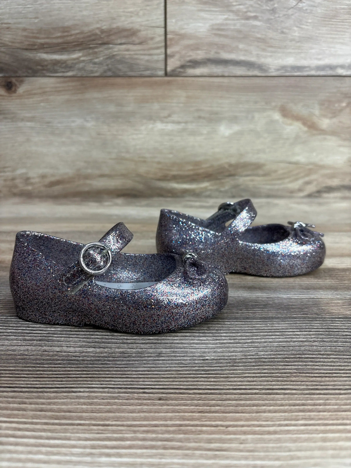 Pair of glittery silver toddler Mary Jane shoes with buckle strap on wood surface