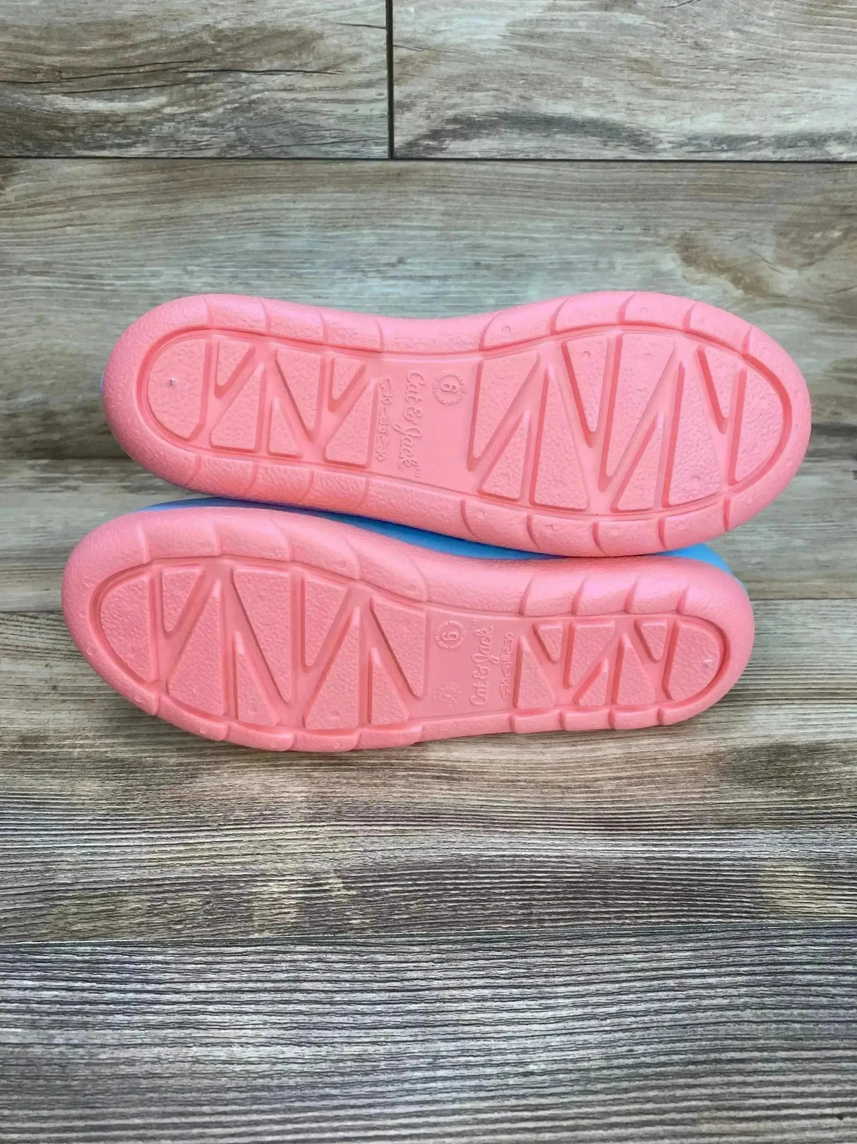 Sole view of Cat & Jack Andy slip-on kids’ rain boots showing pink tread pattern on wooden plank background