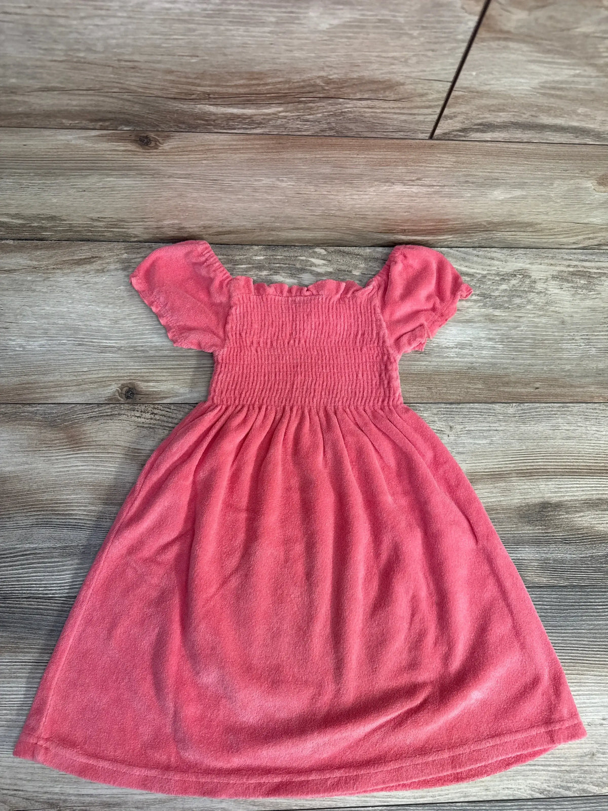 Flat lay of coral Disney Princess terry cloth swim cover dress showing smocked bodice and puff sleeves on wood background