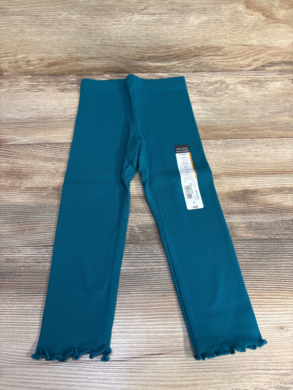 Teal ribbed toddler leggings with lettuce hem, displayed on wood background, clothing tag attached