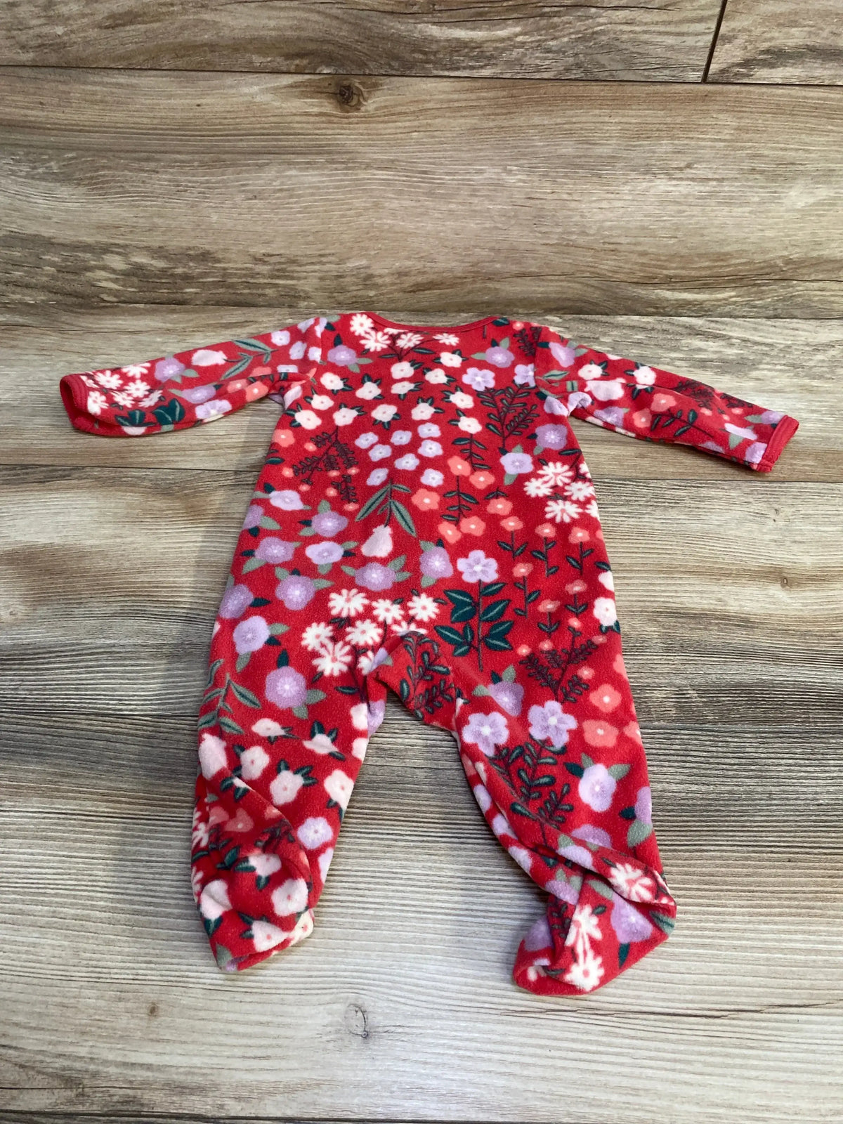 Flat-lay of red Carter’s floral footed blanket sleeper showing long sleeves and all-over pink and lavender flower print on wood background