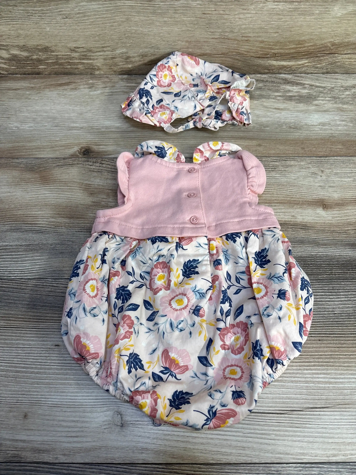Flat lay Tommy Bahama 2-piece bubble romper and bonnet, pink bodice with ruffle sleeves and floral bottom on wood