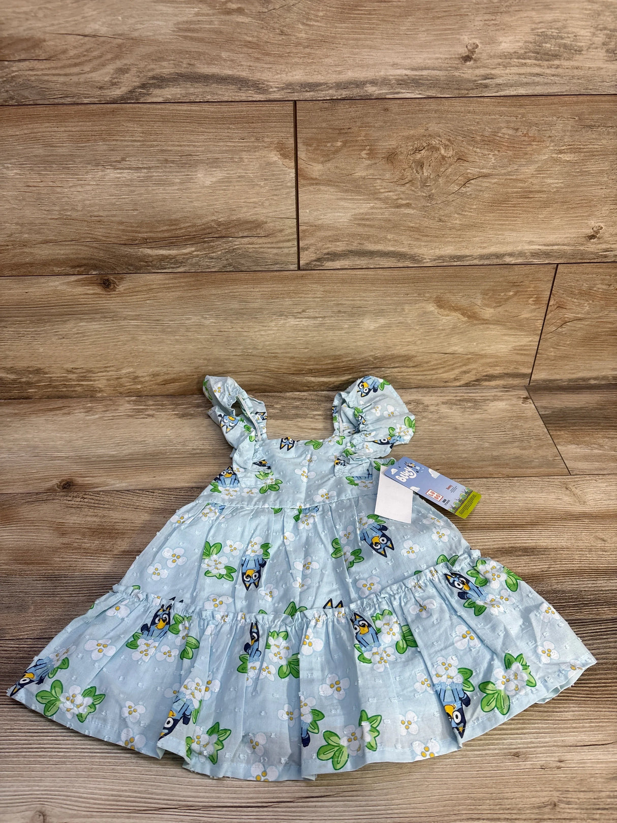 Front flat lay of light blue Bluey Swiss dot toddler dress with ruffled shoulder straps and tiered skirt on wood floor