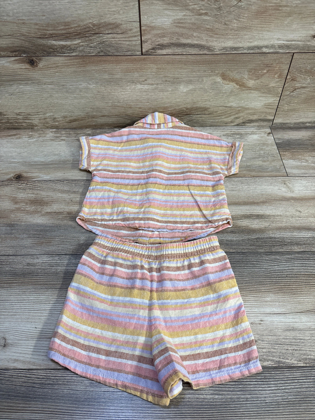 Flat lay of toddler 2-piece linen-blend button-up shirt and elastic-waist shorts with yellow and pastel stripes on wood floor