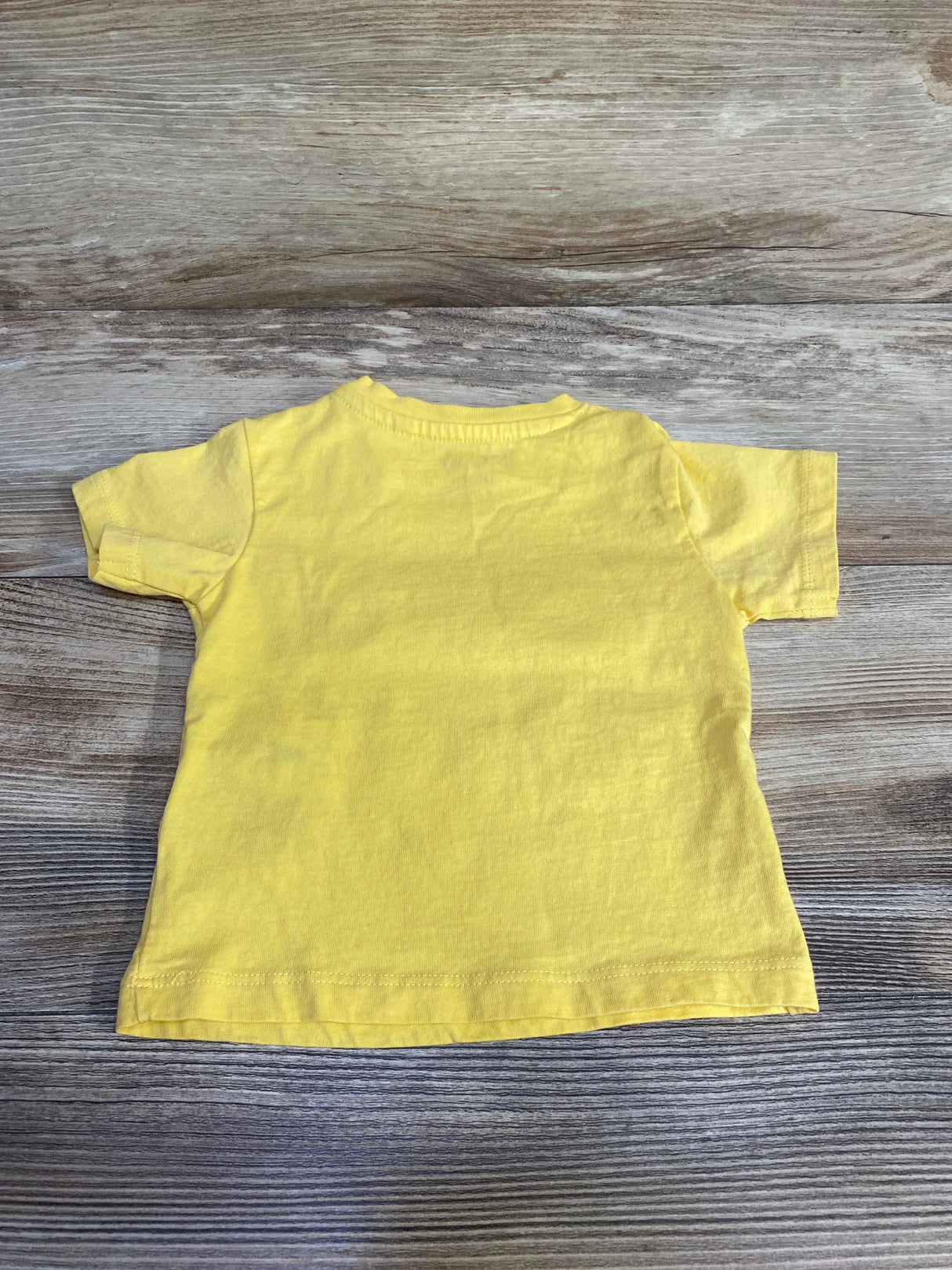 Back view of MO Kids Ciao Buddy baby t-shirt showcasing short sleeves and plain back with wood-grain background