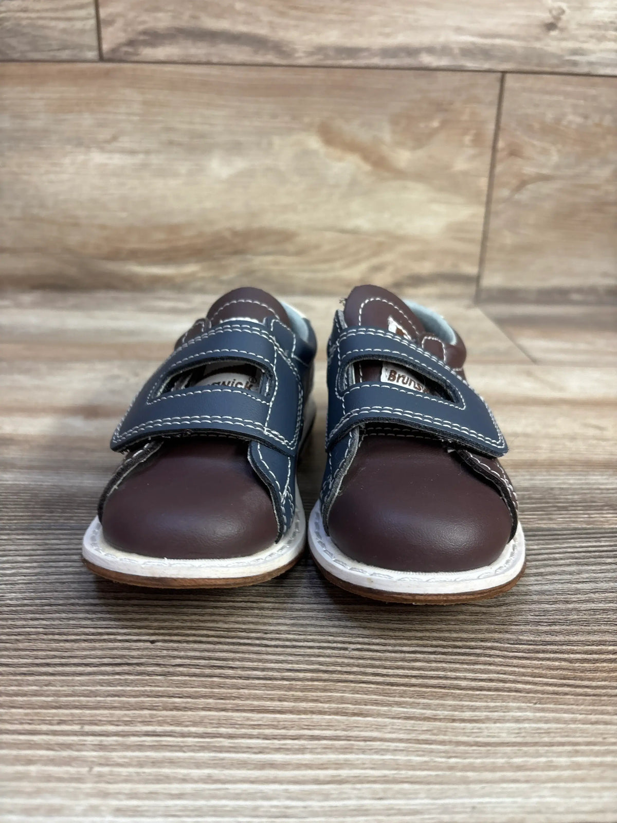 Front view of Brunswick bowling shoes showcasing brown color and hook and loop closures on a wood floor