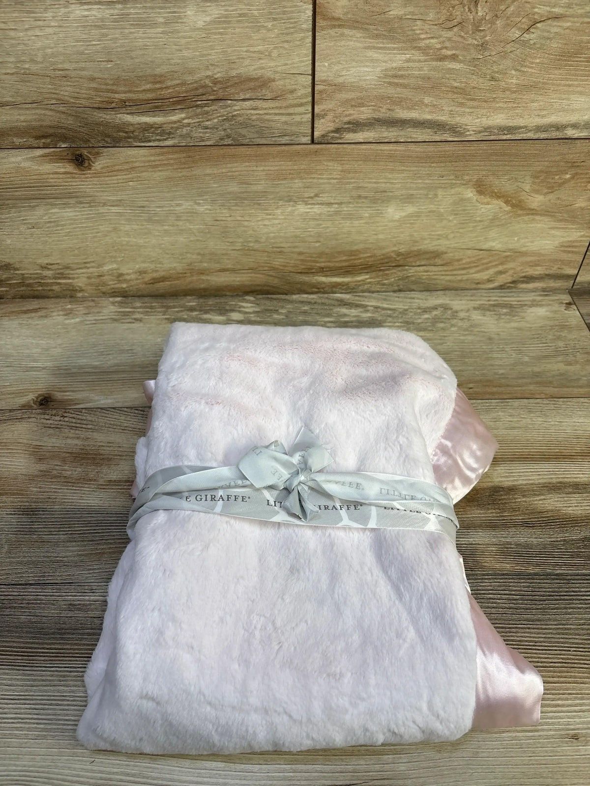 Front view of folded Little Giraffe Luxe baby blanket showcasing pale pink plush pile and satin trim on wood background