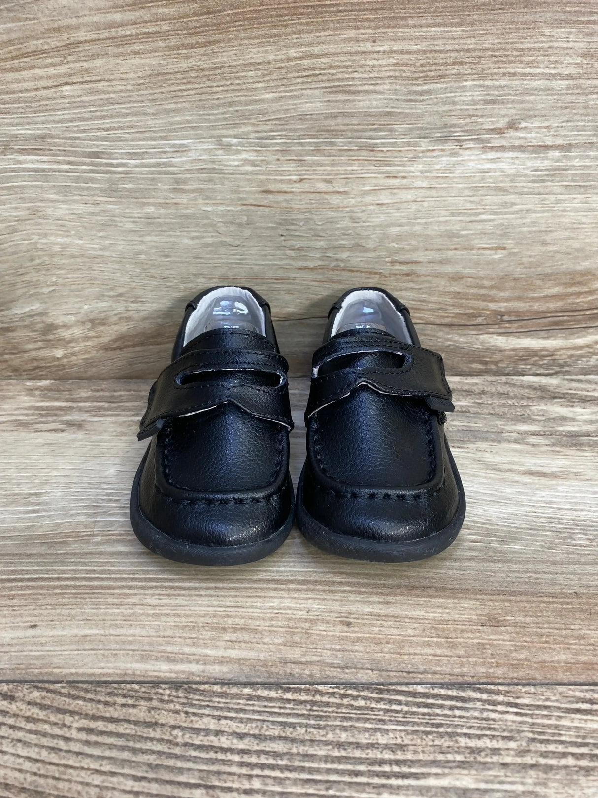 Front view of Pediped Charlie toddler black leather loafers with velcro strap and moc-toe stitching on light wood background