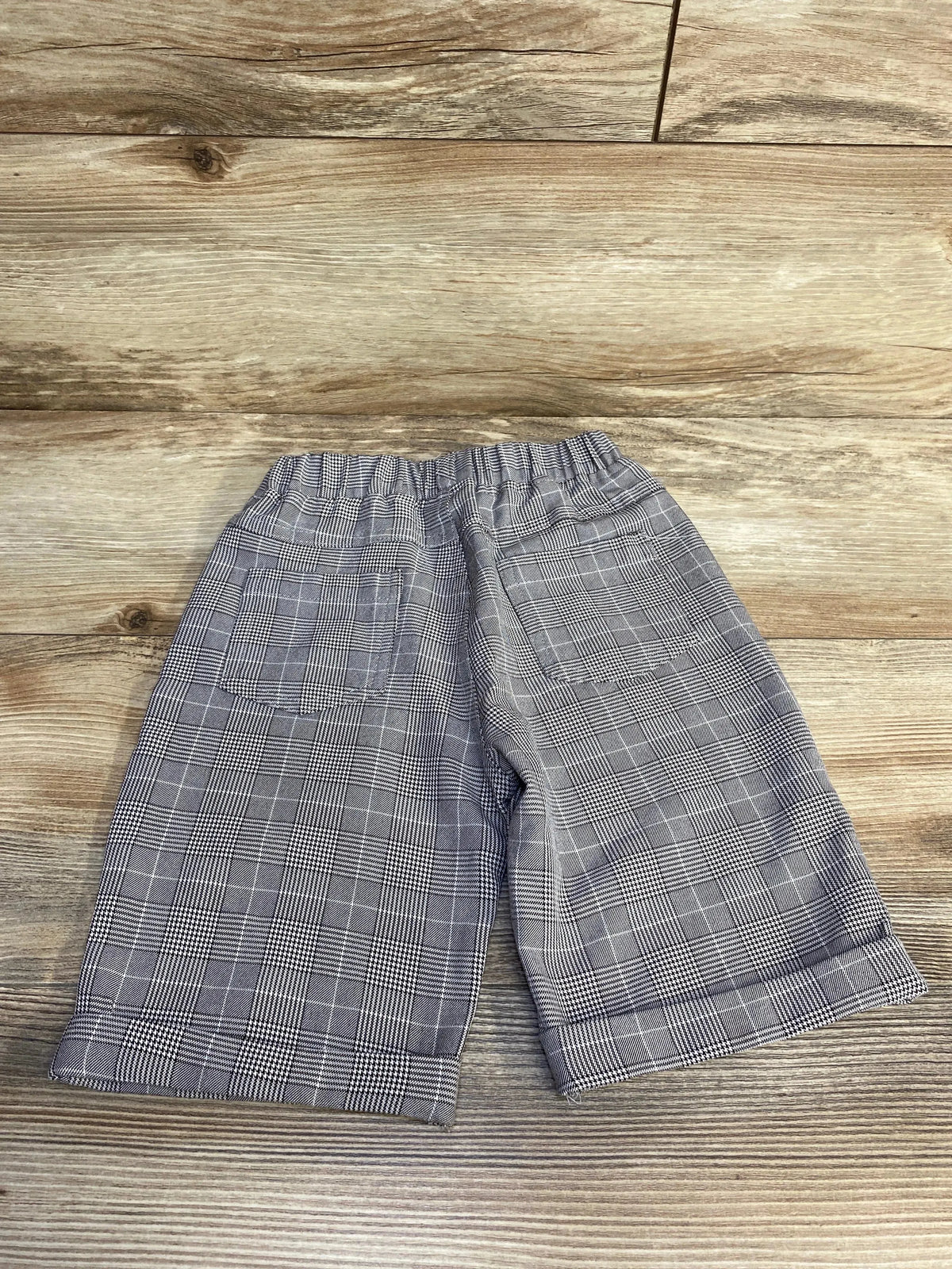 Flat lay of toddler grey plaid pull on shorts with elastic waistband, back patch pockets and cuffed hems on wood background
