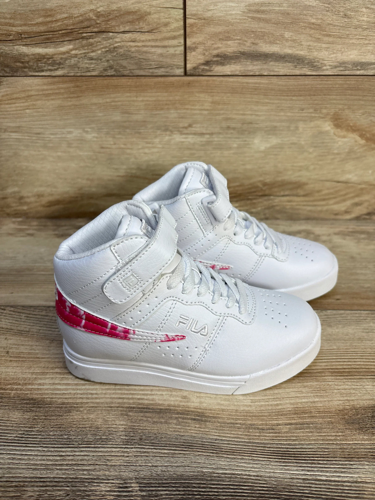 White Fila kids high-top sneakers with pink side detail on wood background