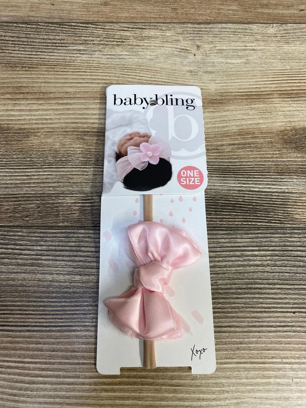 Baby Bling pink bow headband for infants on branded packaging, displayed on wood surface