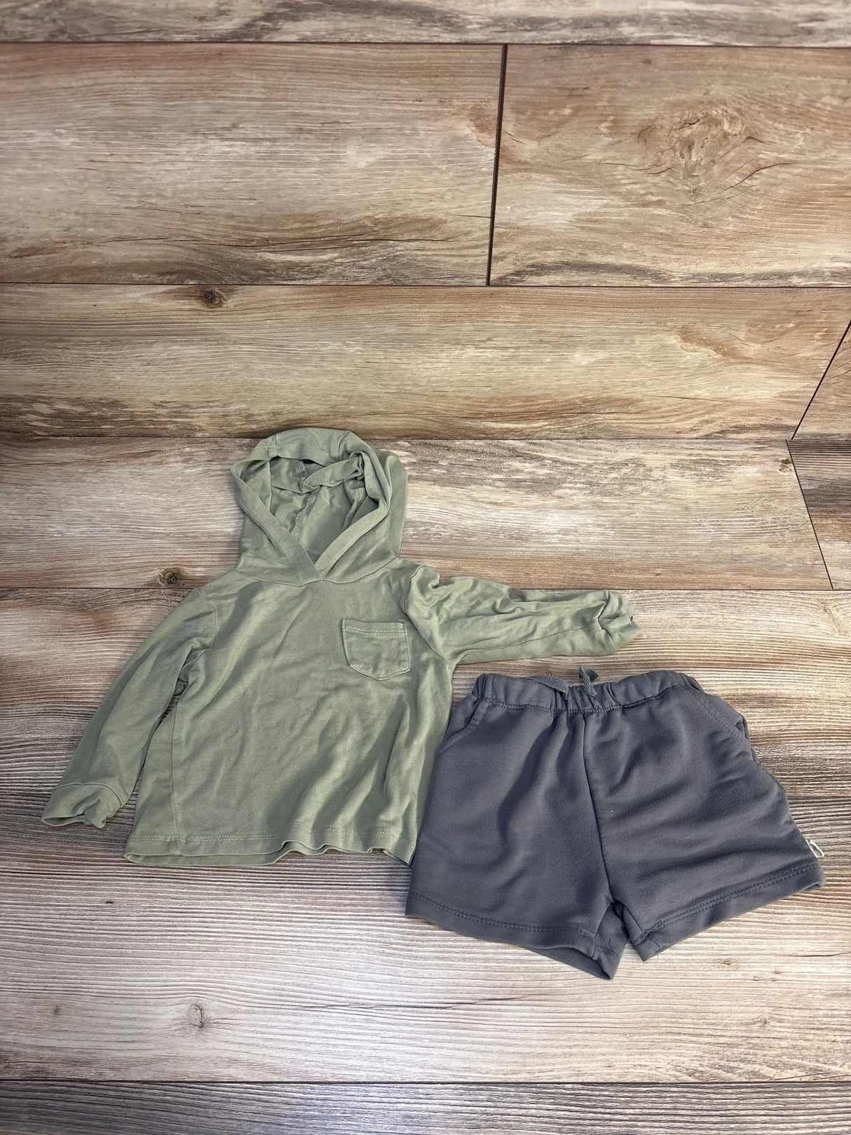 Green long sleeve toddler hoodie with pocket and gray shorts on wood floor