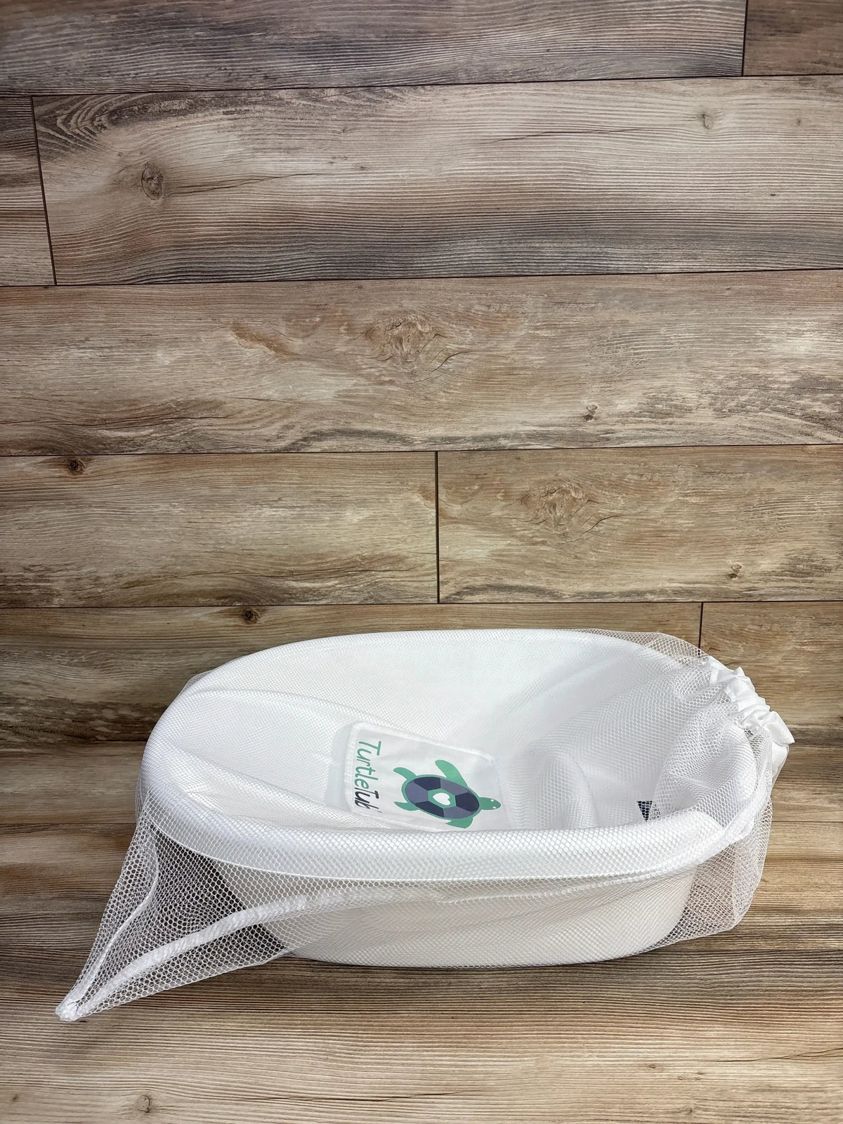 White baby bath tub with mesh cover and turtle graphic on wooden floor
