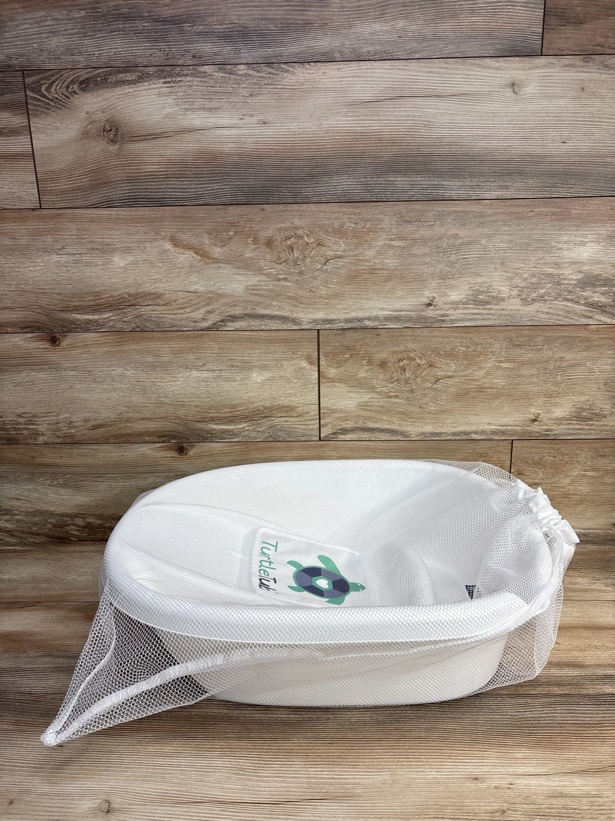 White baby bath tub with mesh cover and turtle graphic on wooden floor