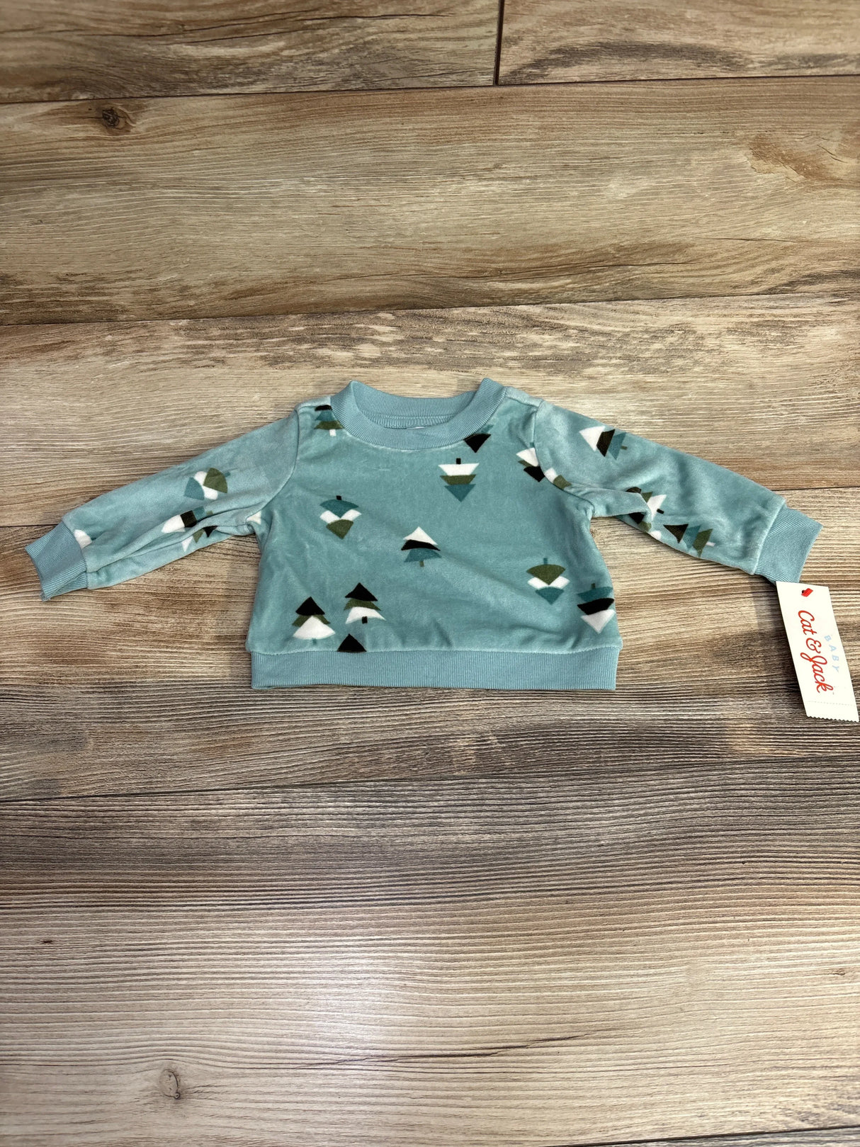 Light blue baby sweatshirt with geometric tree pattern on wooden background