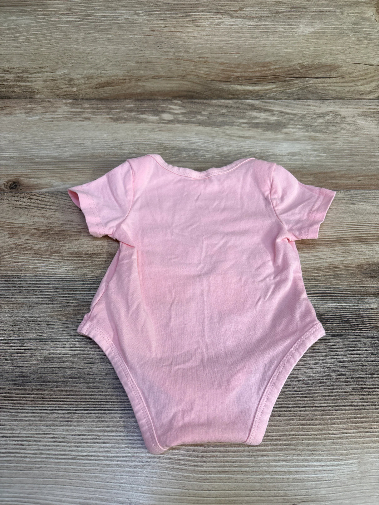 Back view of pink newborn bodysuit (0-3M) showcasing short sleeves and snap crotch on light wood background