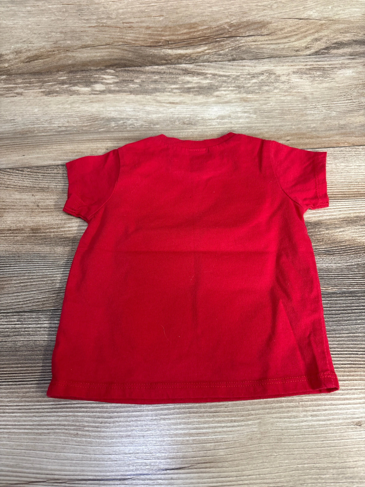 Bright red kids t-shirt laid flat on wood floor, short sleeve children's clothing