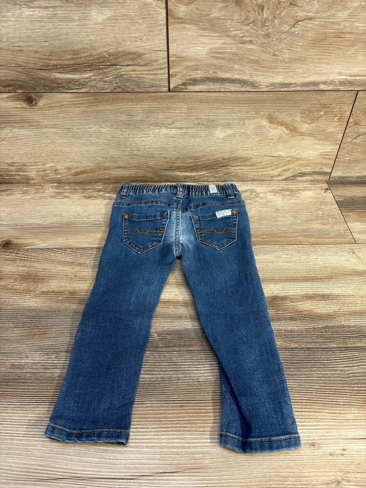 Back view of 7 For All Mankind jeans in size 24 months showcasing two back pockets and an elastic waistband on a wood floor