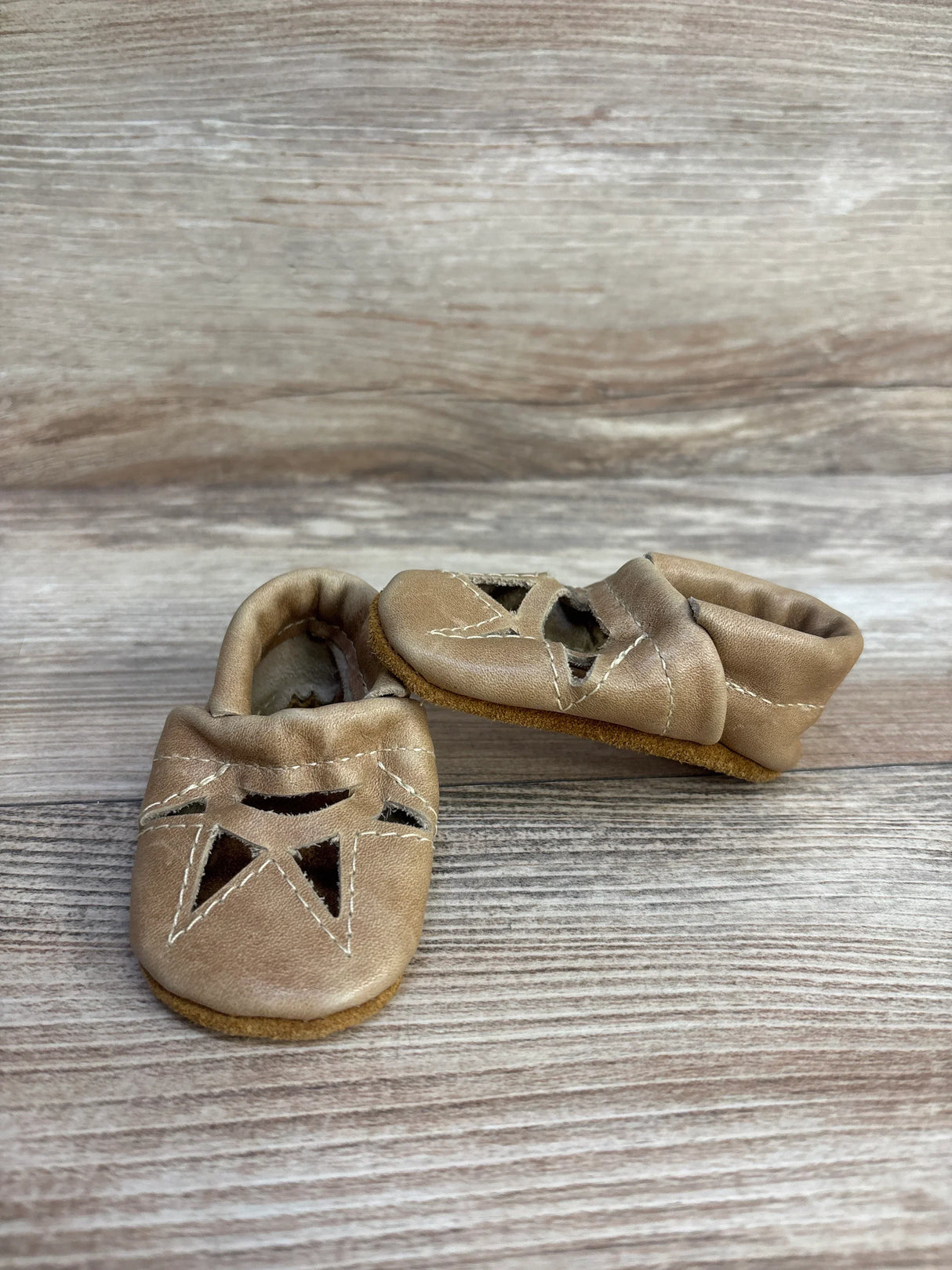 Three-quarter view of baby soft sole leather moccasins sz newborn showcasing tan leather with cut-out star detail on wood plank floor