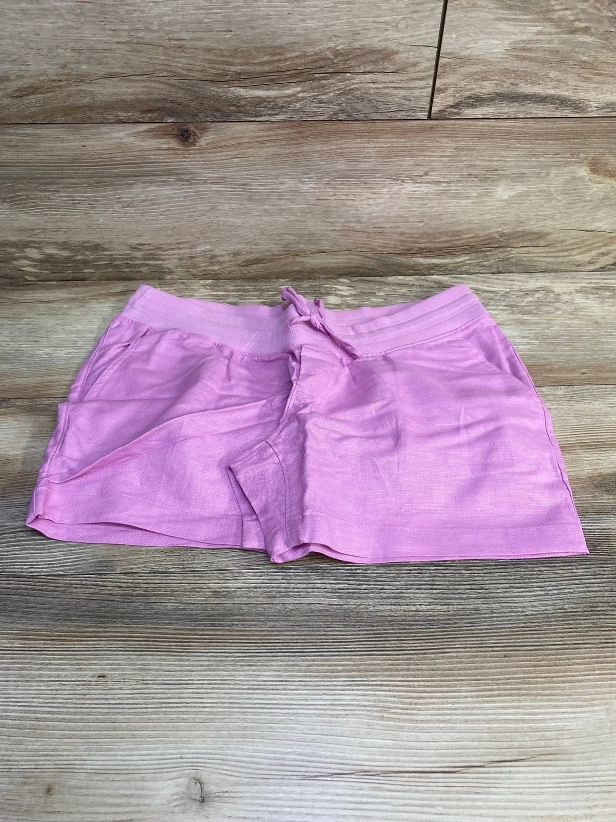 Flat-lay of pink Gap maternity linen-cotton shorts showcasing elastic waistband with drawstring and front pockets on light wood background