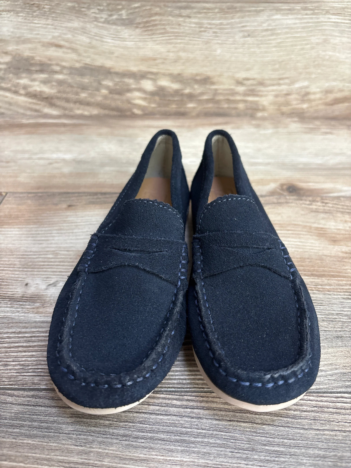Navy suede loafers with white stitching on wooden floor background