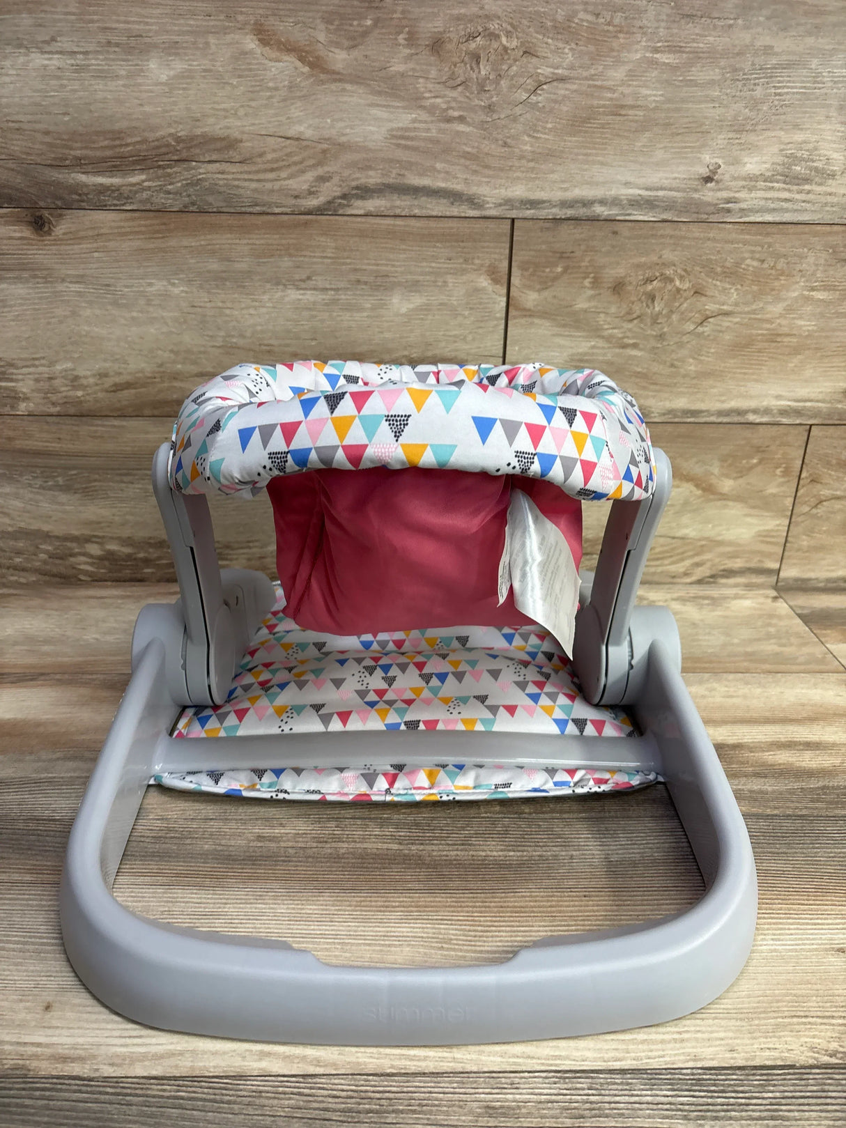 Baby floor seat with gray plastic frame and colorful triangle-patterned fabric on wood background