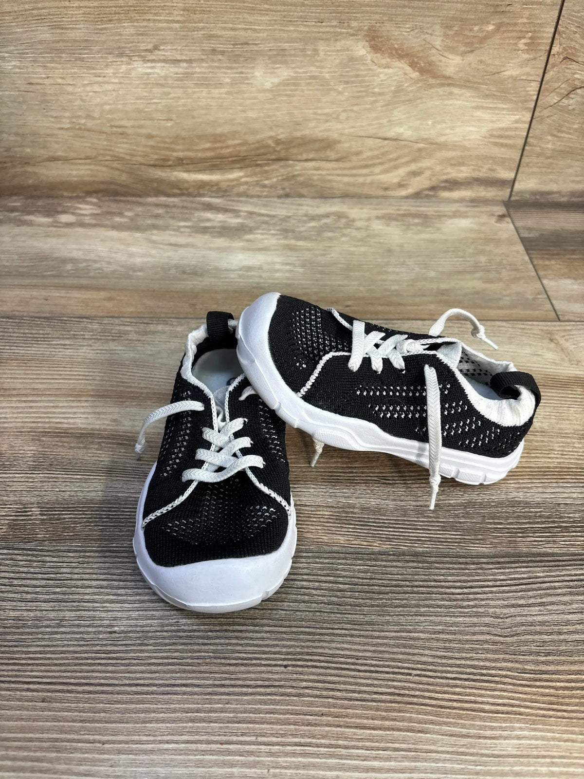 Top and side view of Eqw slip-on sneakers showcasing black uppers and white soles on a wood-look floor