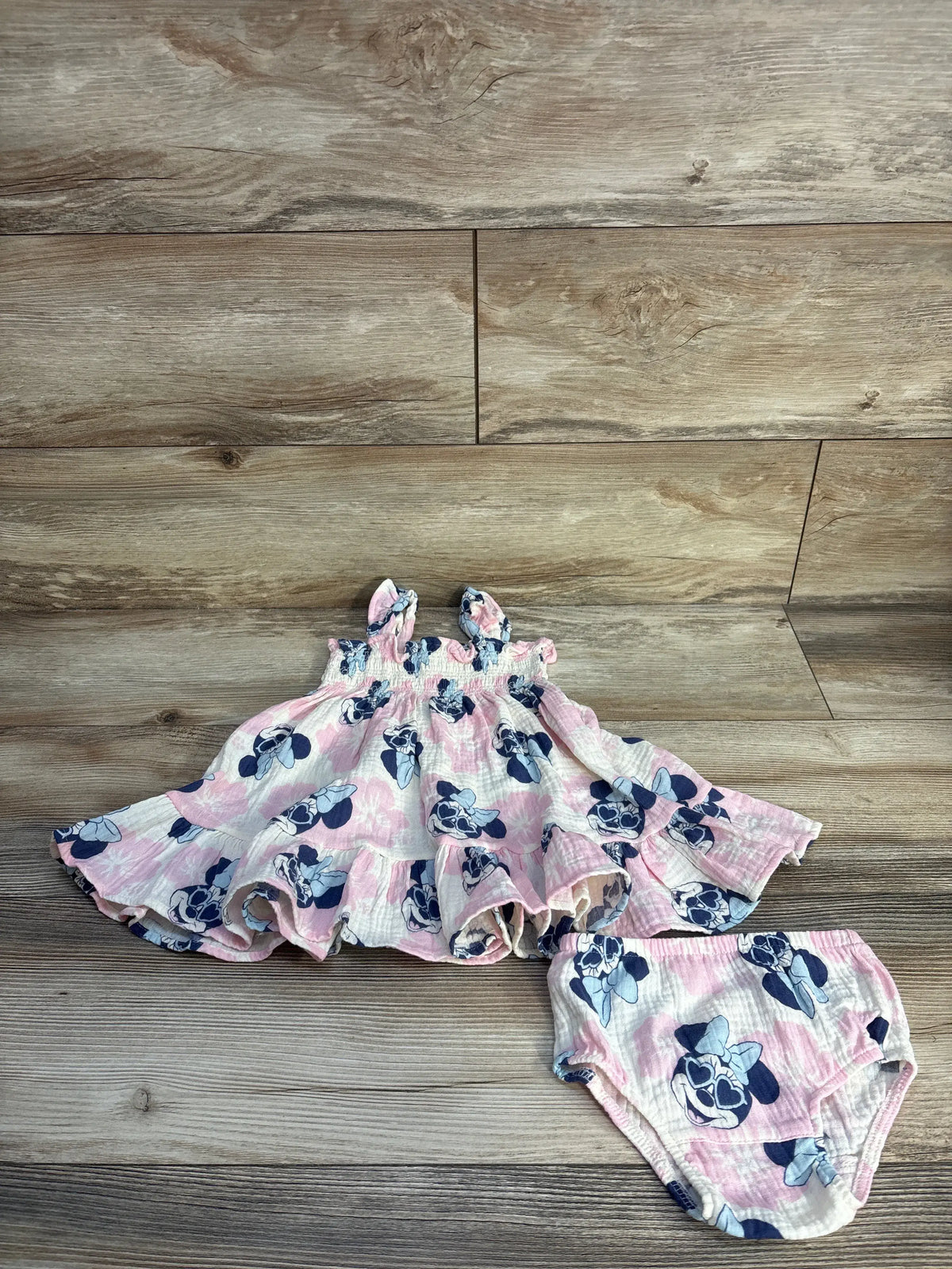 Front view of Disney Baby Minnie Mouse two-piece gauze dress and bloomers set showcasing smocked bodice and peplum hem on wood flooring