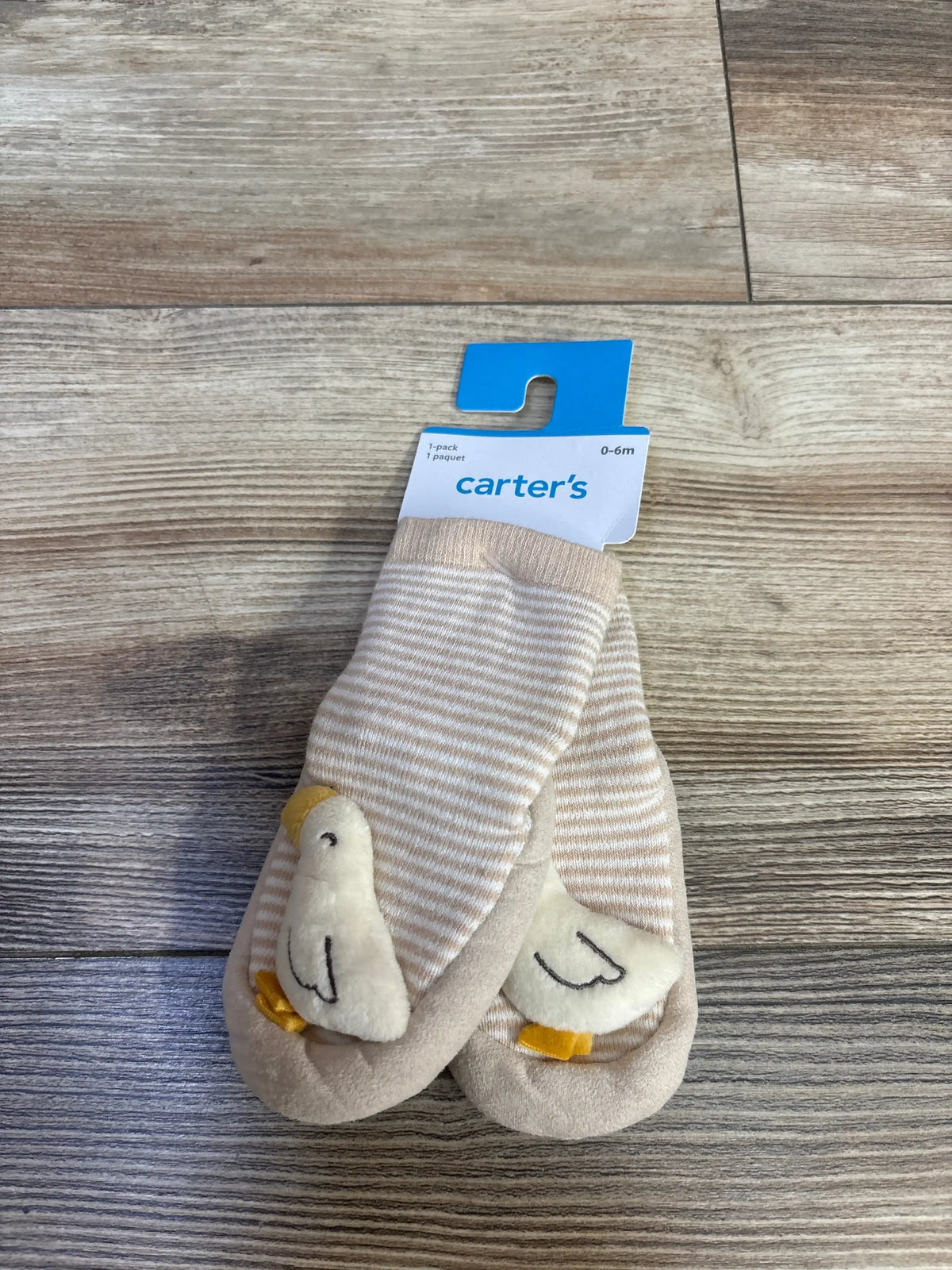 Top view of Carter's beige baby slippers with plush goose rattles on toes on wood floor