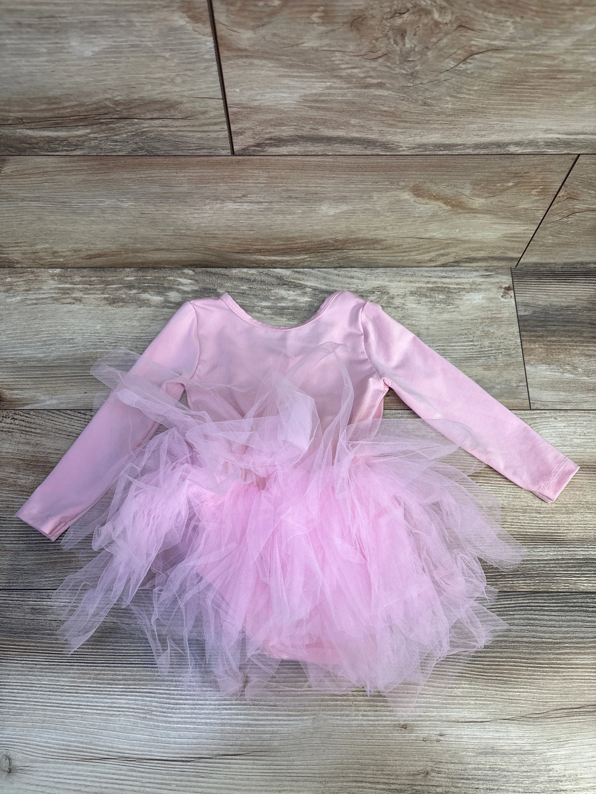 Flat lay of pink long-sleeve tutu leotard showing layered tulle skirt on wood floor, size 4/5T