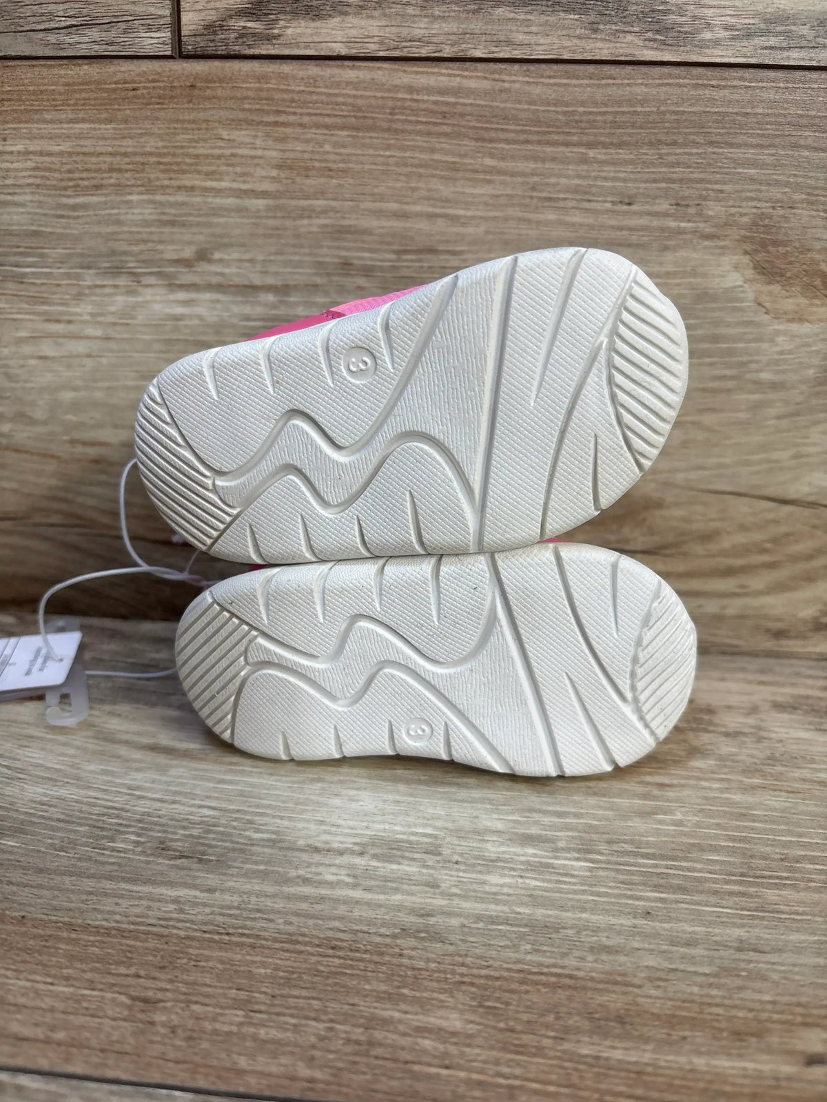 Pair of pink toddler shoes with white non-slip soles on wood background