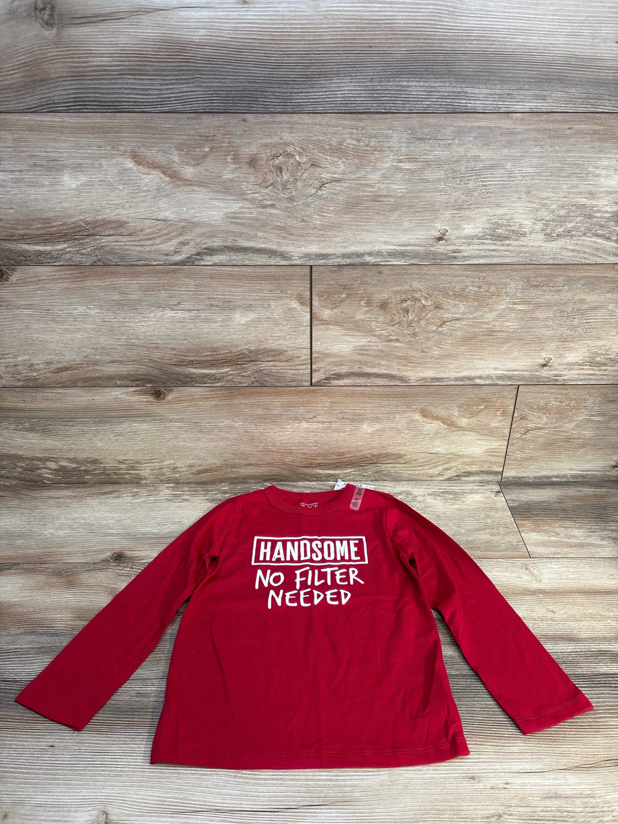 Red kids long sleeve shirt with 'Handsome No Filter Needed' graphic, laid on wood floor