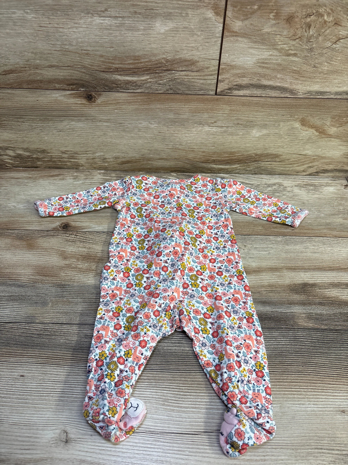 Top view of Simple Joys sleeper in white, size 3 to 6 months, with floral pattern and covered feet on wood flooring