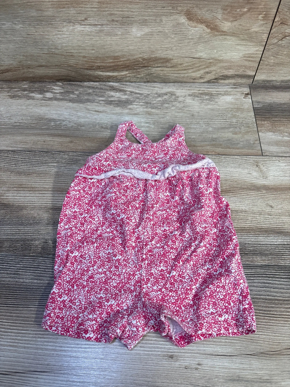 Flat lay of pink Carter’s tank romper 6M with sleeveless halter top, ruffle trim, and small white floral print on wood floor