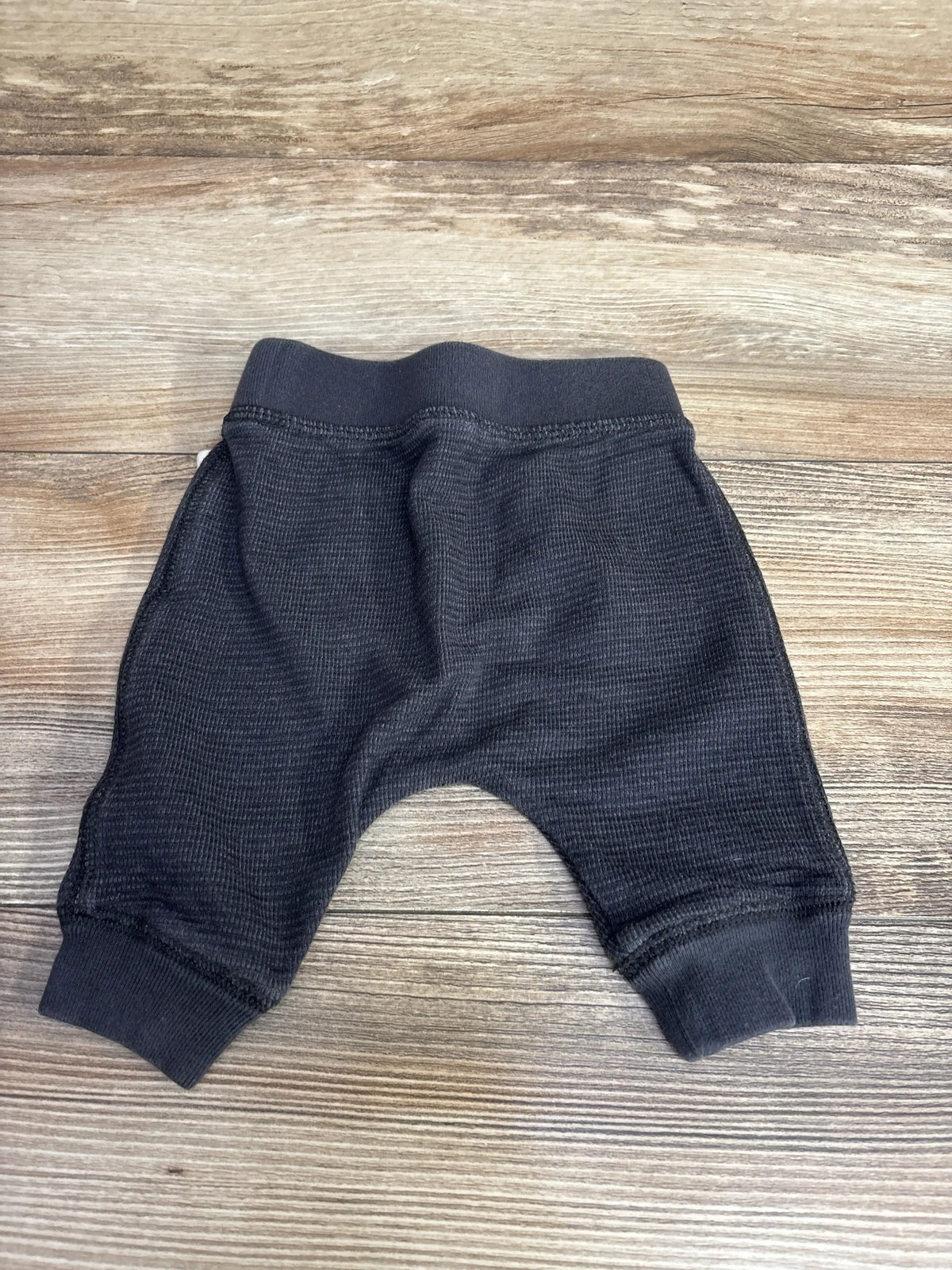 Top-down view of newborn grey waffle knit drawstring pants showing ribbed waistband and cuffs on wooden surface
