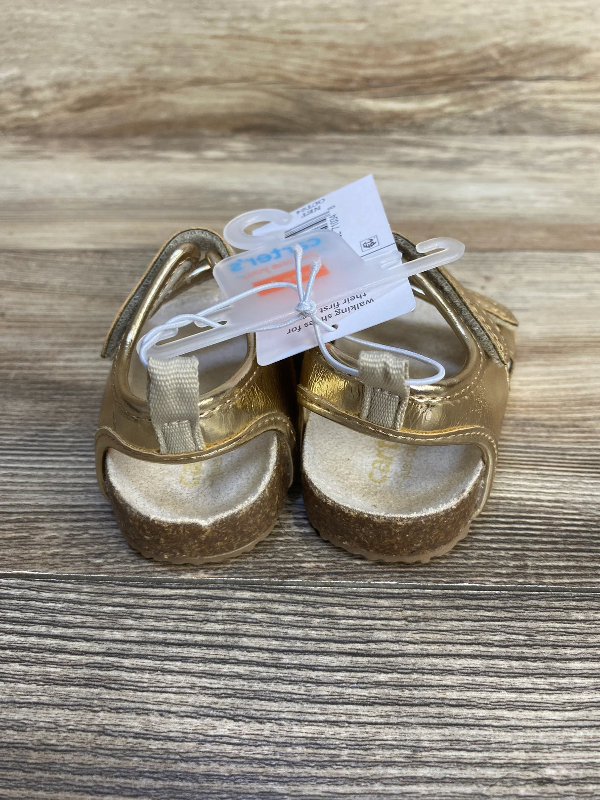 Gold toddler sandals with cork soles and Velcro straps on a wood surface