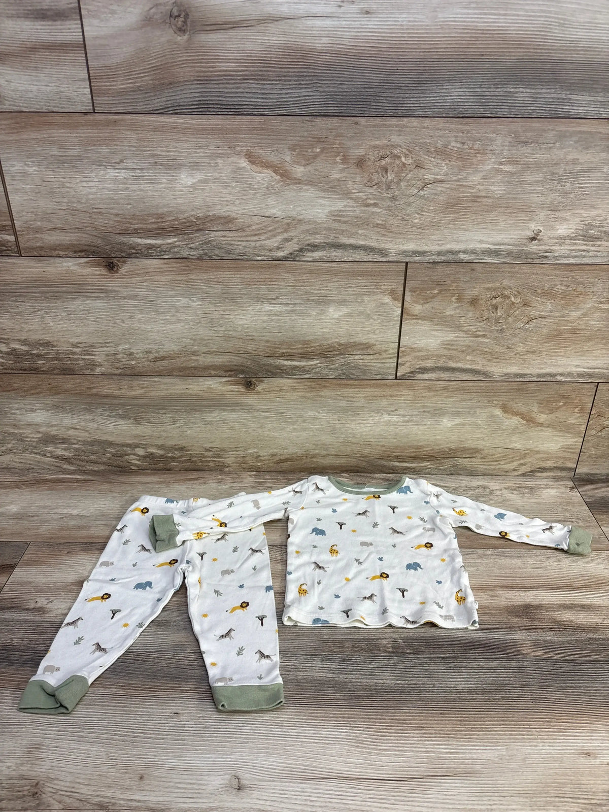 Flat lay of Mori Baby 2Pc Safari Pajama Set ivory sz 9-12m showcasing safari print with sage cuffs on wood plank floor